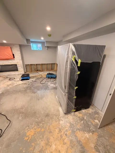 Basement drying with the fridge wrapped in plastic and the lower drywall removed