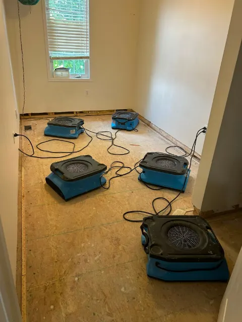 Five air movers drying a bedroom subfloor after the carpet and baseboards were removed