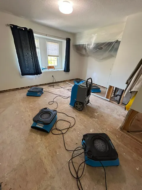 LGR dehumidifier and air movers drying a bedroom after a flood cut, with plastic sheeting protecting the wall