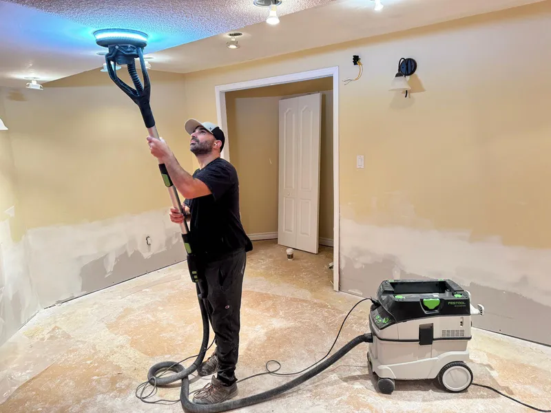 Festool drywall sander with HEPA vacuum attachment during post-fire ceiling restoration