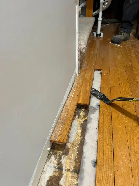 Technician lifting water-damaged hardwood along a hallway wall