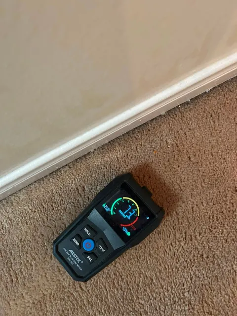 Moisture meter reading 73 on drywall at the baseboard during a water damage inspection