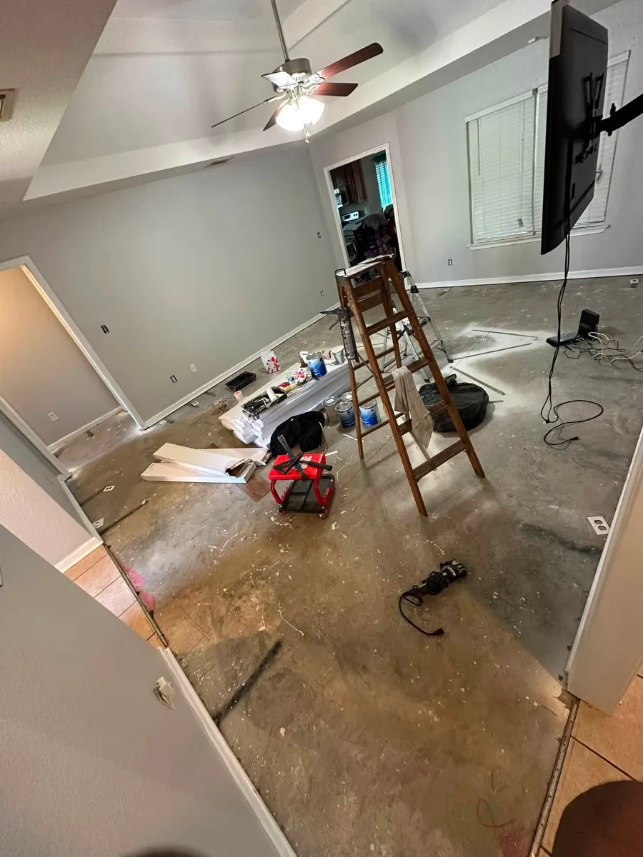 Room stripped to the subfloor with a ladder and tools mid-repair
