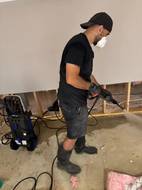 Technician cleaning the exposed wall cavity after the lower drywall was removed