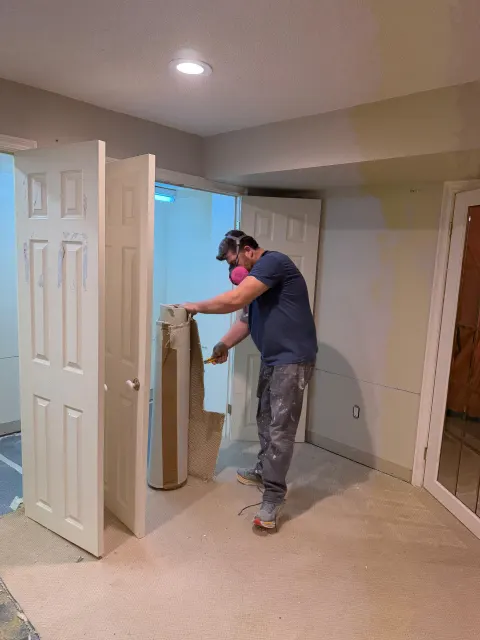 Technician cutting out damaged drywall beside a doorway