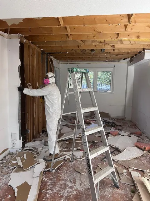 Technician in a Tyvek suit removing ceiling and wall drywall