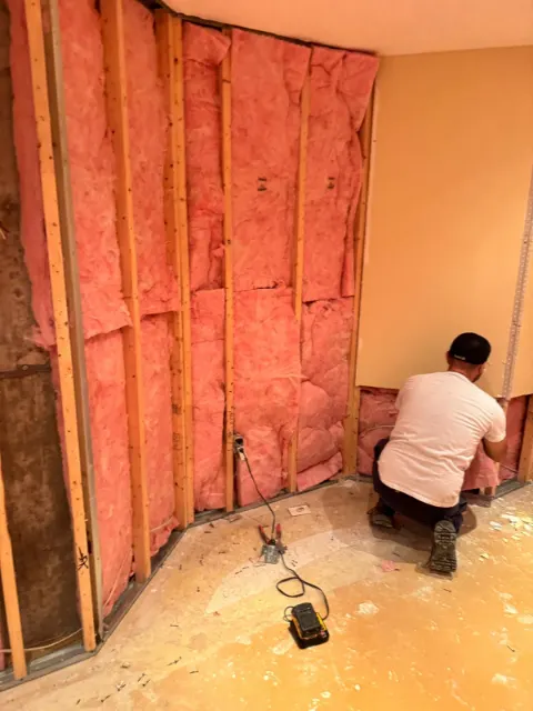 Technician fitting new insulation into exposed wall framing during the rebuild