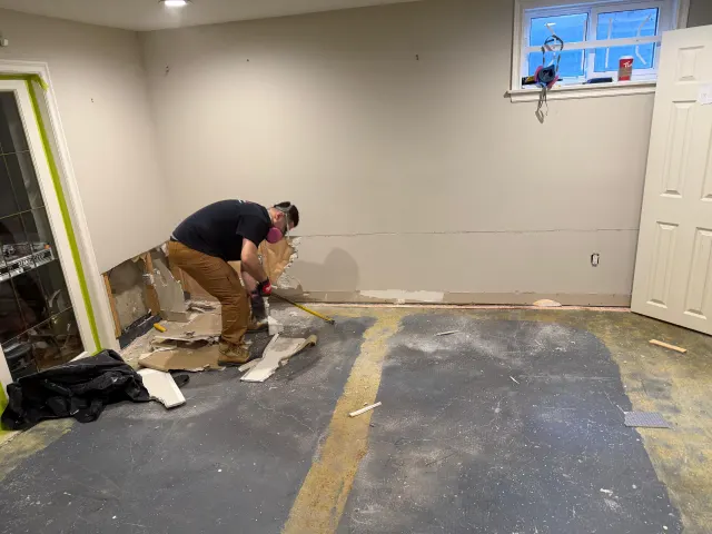 Technician pulling baseboard and damaged drywall from a basement wall