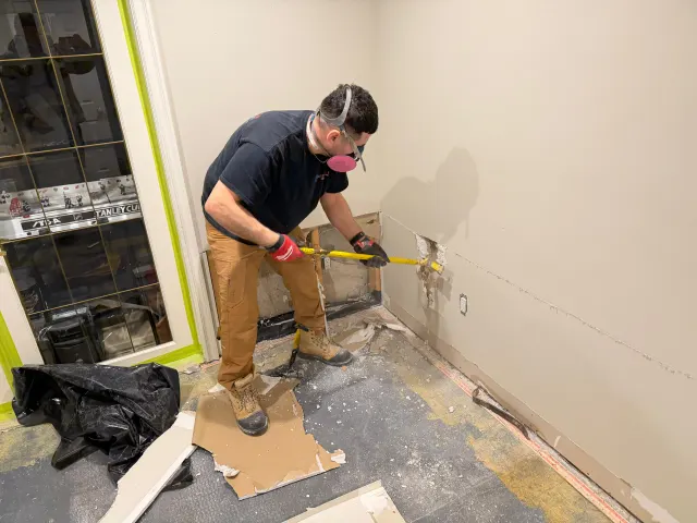 Technician in a respirator removing water-damaged drywall