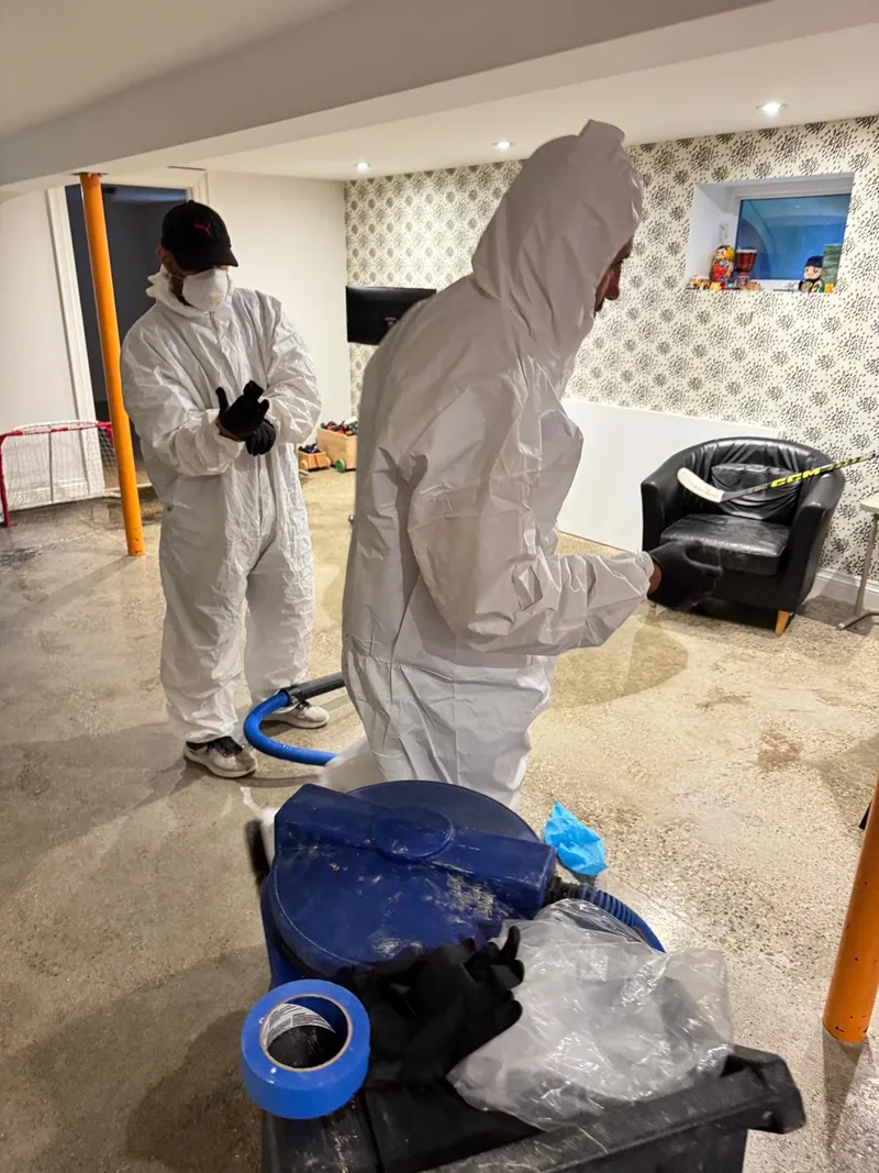 Two technicians in full Tyvek performing Category 3 water remediation on basement concrete